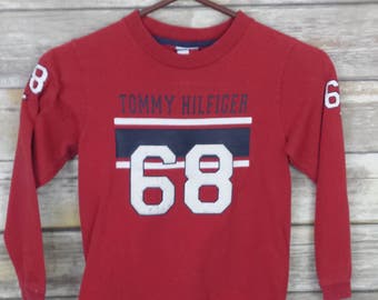 May include: Red long-sleeve shirt with a white and blue Tommy Hilfiger logo and the number 68 on the front.
