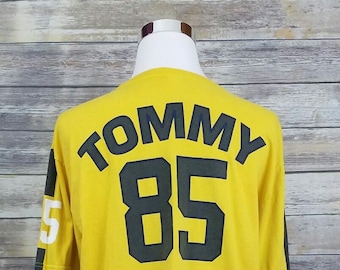 May include: A yellow long-sleeve t-shirt with navy blue sleeves. The back of the shirt has the word "TOMMY" and the number "85" printed in black.