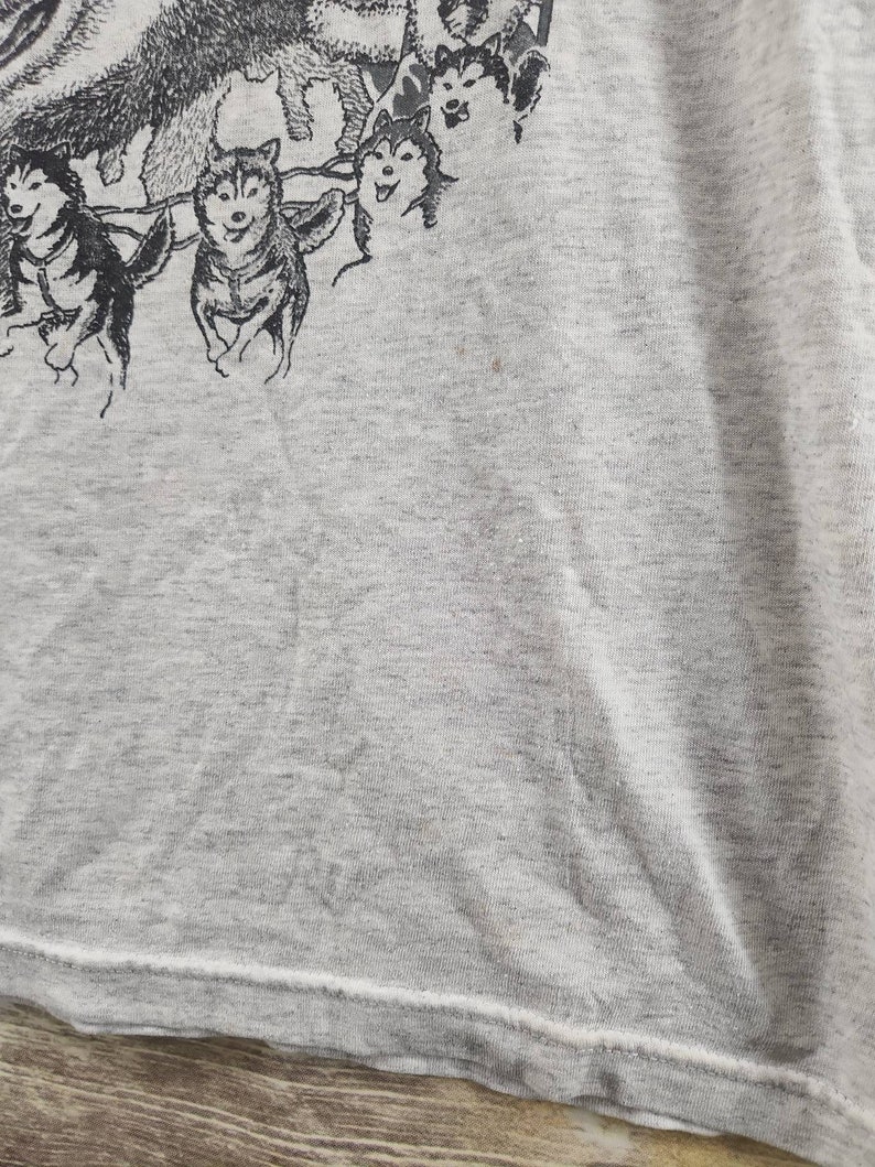 May include: A gray t-shirt with a black and white illustration of a team of sled dogs pulling a sled.
