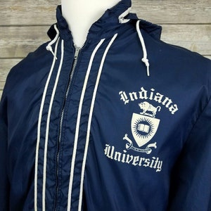 May include: A navy blue hooded jacket with white piping and a white embroidered Indiana University logo on the front. The logo features a shield with a book, a sun, and a bull.