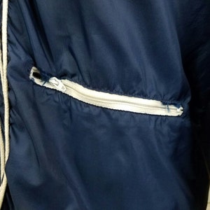 May include: A navy blue jacket with a white zippered pocket. The jacket has a drawstring at the neck.