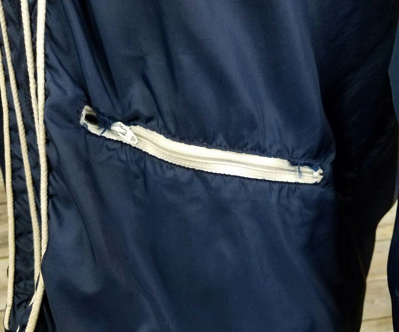May include: A navy blue jacket with a white zippered pocket. The jacket has a drawstring at the neck.
