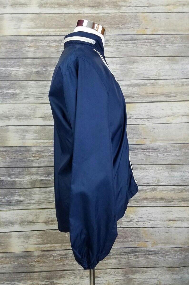 May include: A navy blue windbreaker jacket with white piping along the collar, zipper, and cuffs.