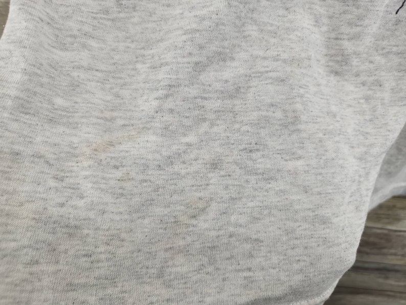 May include: Close-up of a light gray fabric with a subtle texture. The fabric has a few faint brown stains.
