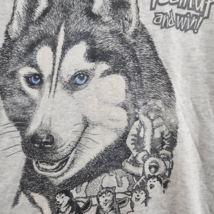 May include: A gray t-shirt with a black and white illustration of a husky dog pulling a sled. The text "Team Up and Win!" is printed on the shirt.