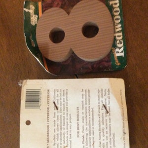 May include: A wooden number eight, made from redwood, is packaged in a plastic bag with a green and white label that reads "Genuine Redwood". The label also includes the text "SIGNS ADDRESSES INTERIOR EXTERIOR".