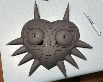 May include: A black 3D printed mask with a heart shape and sharp spikes. The mask has two large eye holes and a detailed design.
