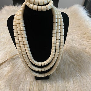 May include: A white beaded necklace and bracelet set. The necklace is made of multiple strands of large, round beads. The bracelet is a single strand of the same beads.