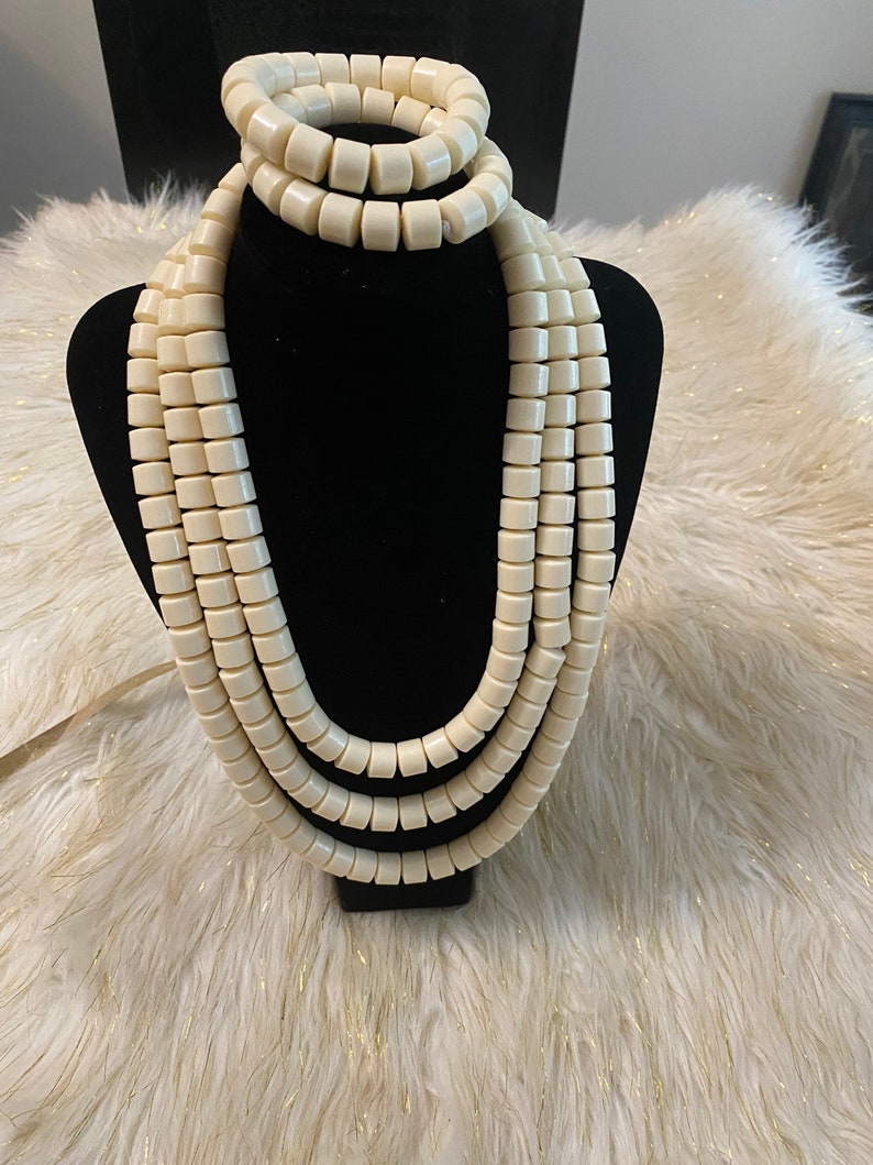 May include: A white beaded necklace and bracelet set. The necklace is made of multiple strands of large, round beads. The bracelet is a single strand of the same beads.