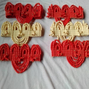 May include: A set of six beaded headbands, three red and three cream colored, with gold beads interspersed throughout. The headbands are arranged in two rows of three, with the red headbands on top and the cream headbands on the bottom.