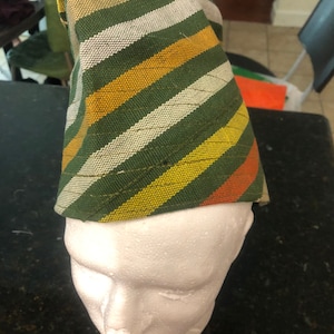 May include: A green, yellow, orange, and white striped fabric hat. The hat is on a white styrofoam head.