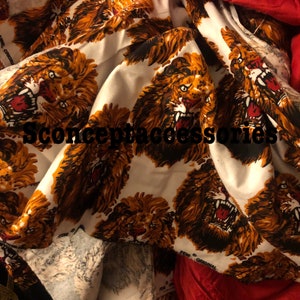 May include: White fabric with a repeating pattern of orange and brown lions with black outlines. The lions have open mouths and sharp teeth. The fabric is folded and crumpled.