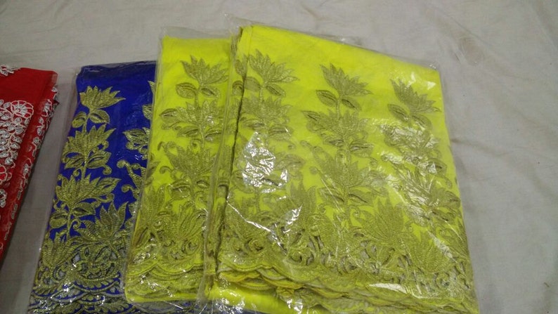 Puede incluir: Primer plano de varias piezas de tela en rojo, azul y amarillo. Cada pieza est&aacute; bordada con un dise&ntilde;o floral en dorado. La tela est&aacute; empaquetada en pl&aacute;stico transparente, lo que sugiere que es nueva y est&aacute; lista para usar. El tema general es textil.