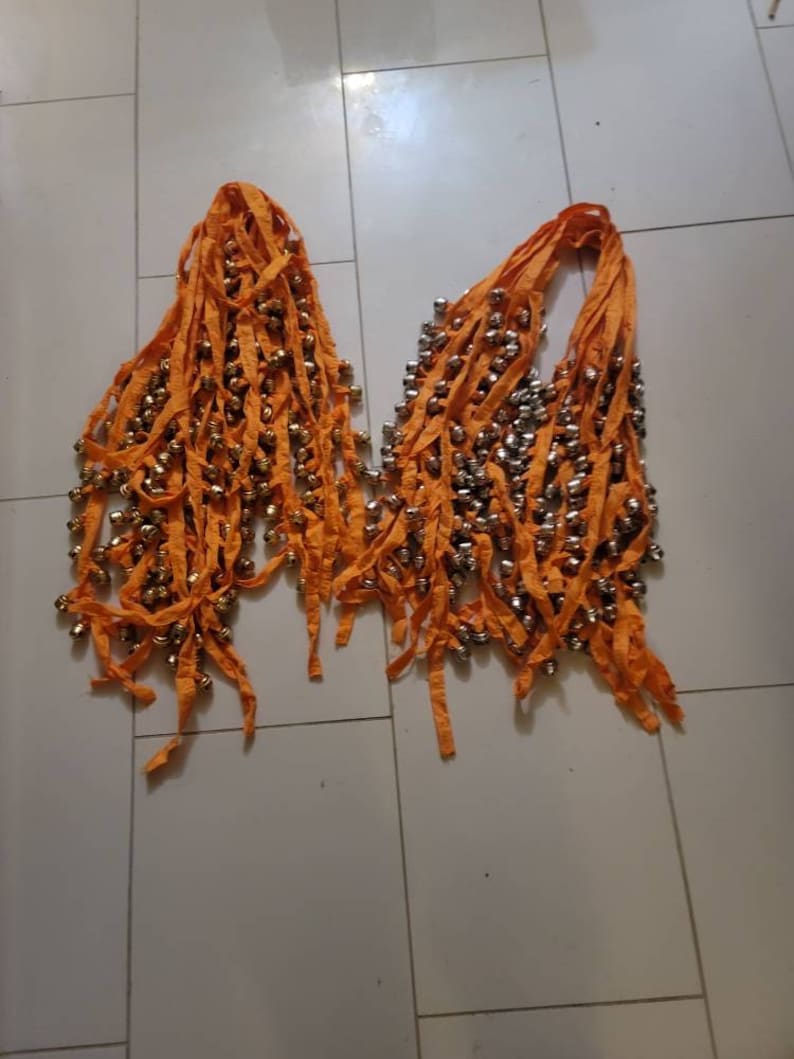 Op de afbeelding: Twee oranje stoffen stroken met rijen kleine zilveren belletjes. De stroken zijn aan de bovenkant aan elkaar gebonden.