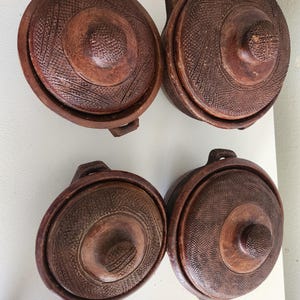 Op de afbeelding: Vier handgemaakte, bruine keramische kookpotten met deksels. Elke pot heeft een getextureerd, patroonontwerp op het deksel en de body, met een klein handvat aan elke kant. De deksels hebben een centrale knop. Ideaal om in te koken en te serveren.