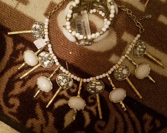Puede incluir: Un collar de oro con colgantes de piedra blanca y negra y una pulsera a juego de oro y blanco. La pulsera tiene una etiqueta con el texto "#48000 GPTIV".