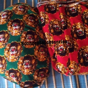 May include: Two fabric swatches with a repeating pattern of lion faces. One swatch is green with gold lions, the other is red with gold lions. The text "Sconceptaccessories" is printed on the green swatch.
