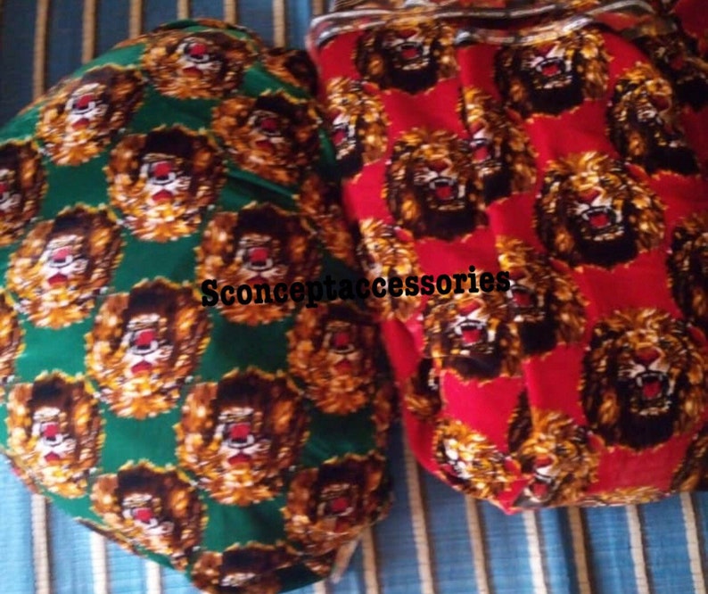 May include: Two fabric swatches with a repeating pattern of lion faces. One swatch is green with gold lions, the other is red with gold lions. The text "Sconceptaccessories" is printed on the green swatch.