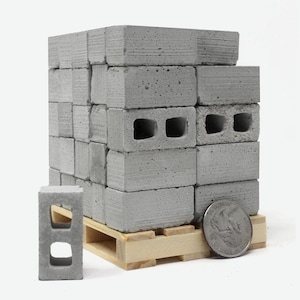 May include: A miniature stack of gray concrete cinder blocks on a wooden pallet with a US quarter for scale. The blocks have holes for ventilation.