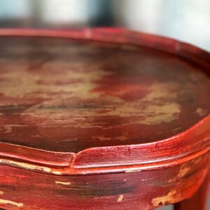 May include: Close-up of a red wooden table top with a distressed finish. The table top has a rounded edge and a slightly uneven surface.