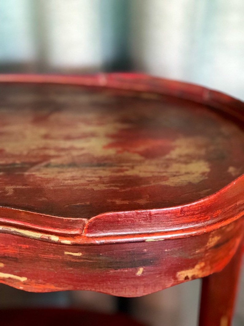 May include: Close-up of a red wooden table top with a distressed finish. The table top has a rounded edge and a slightly uneven surface.