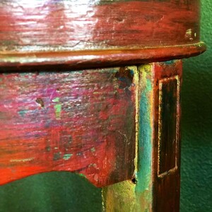 May include: Close-up of a wooden table leg with red, green, and gold paint. The leg has a rectangular groove and a small hole.