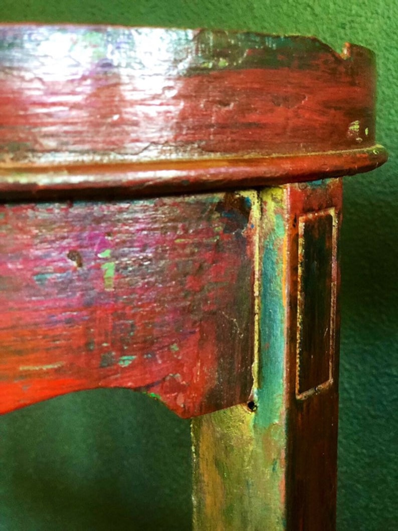 May include: Close-up of a wooden table leg with red, green, and gold paint. The leg has a rectangular groove and a small hole.