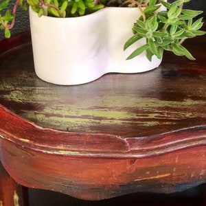 May include: A white ceramic planter shaped like a heart with two succulents growing inside. The planter is sitting on a dark wooden table with a distressed finish.