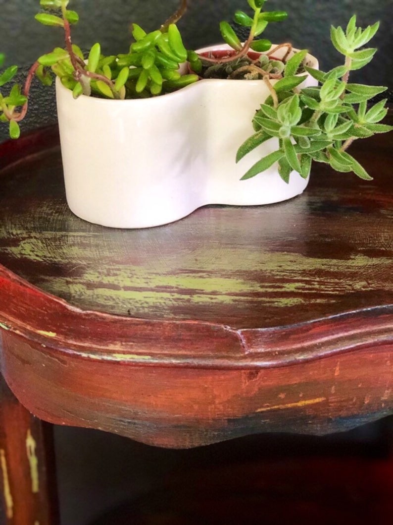 May include: A white ceramic planter shaped like a heart with two succulents growing inside. The planter is sitting on a dark wooden table with a distressed finish.