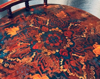 May include: Round wooden tray with a handle, featuring a distressed finish. The tray is painted with a detailed floral pattern in shades of red, blue, and gold. The handle is curved and attached with small, decorative posts.