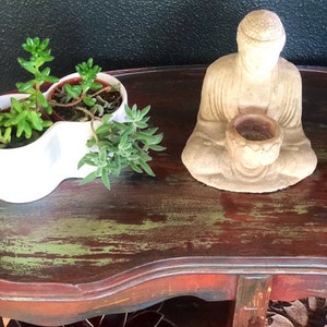 May include: A small, distressed wooden table with a green and red finish. The table has a shelf and is decorated with a small Buddha statue and potted succulents.