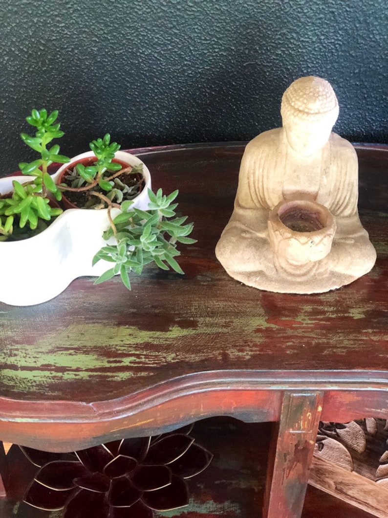 May include: A small, distressed wooden table with a green and red finish. The table has a shelf and is decorated with a small Buddha statue and potted succulents.