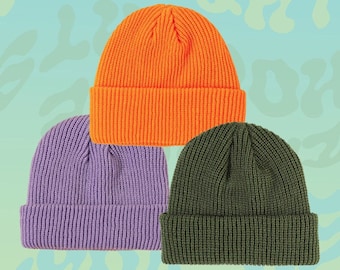 May include: Three knitted beanies in different colors: orange, purple, and green. The beanies are folded and stacked on top of each other.