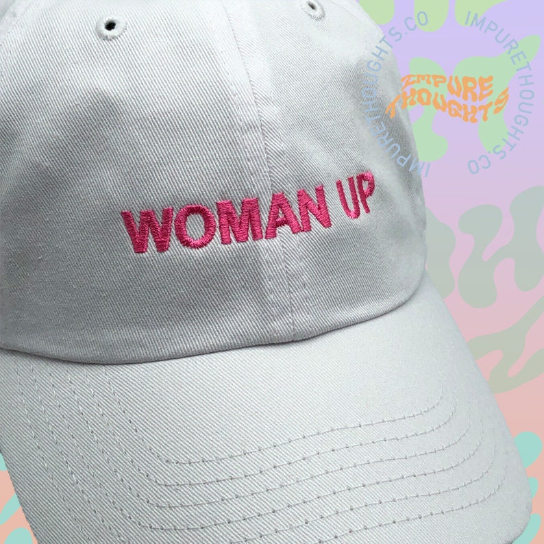 May include: A gray baseball cap with the phrase "WOMAN UP" embroidered in pink on the front.