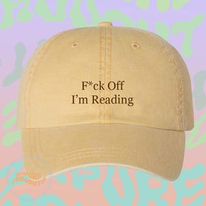 May include: A light yellow baseball cap with a distressed, washed-out finish. The front panel features the dark brown embroidered text F*ck Off I’m Reading. The cap has a structured crown, a curved brim, and visible stitching along the panels.