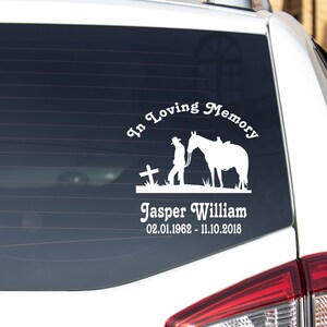 May include: White vinyl decal applied to a car window. The decal features a cowboy with a horse, a cross, and the text "In Loving Memory" above the name "Jasper William" and dates 02.01.1962 - 11.10.2018.