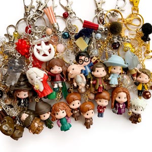 May include: A collection of metal keychains featuring various miniature plastic character figurines, including figures with glasses, capes, and hats. The keychains are adorned with colorful beads, small tassels, and silver-toned lobster claw clasps.