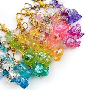 May include: A collection of colorful translucent character keychains featuring various figures in shades of blue, green, yellow, orange, pink, and purple. Each keychain includes a metal lobster clasp, a split ring, and small decorative beads.