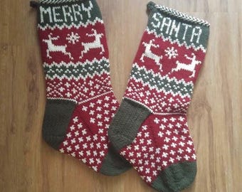 May include: Two knitted Christmas stockings. One stocking reads "MERRY" and the other reads "SANTA" in white letters. Both stockings have a red background with white and green patterns, including reindeer and snowflakes. The toe and cuff are green.