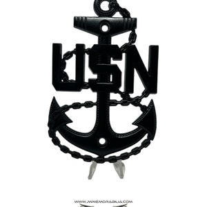 May include: Black metal anchor with the letters "USN" integrated into the design. The anchor is detailed with chain links and is displayed on a clear stand. The image includes the website address and social media handles.