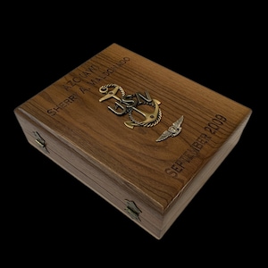 May include: A wooden box with a brass anchor and wings engraved with "AZC (AW) SHERRY A. MALDONADO SEPTEMBER 2009".