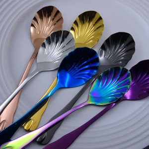 Puede incluir: Conjunto de seis cucharas de acero inoxidable de colores con un diseño en forma de concha. Las cucharas están dispuestas en forma de abanico sobre una superficie blanca.