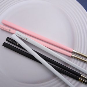 May include: Four pairs of chopsticks with silver tips. Two pairs are black, one pair is white, and one pair is pink. Each chopstick has the words "Love you!" engraved on them.
