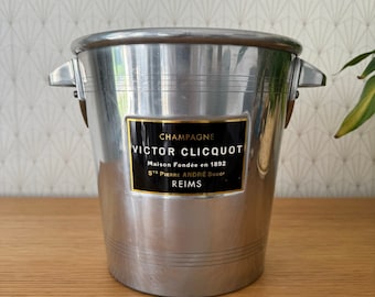 May include: Silver champagne bucket with a black and gold label that reads "Champagne Victor Clicquot Maison Fondée en 1892 St Pierre André Succeur Reims".