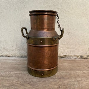 May include: A copper milk can with a brass lid and handle. The can has a chain attached to the lid.