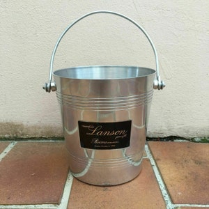 Op de afbeelding: Zilveren champagne-emmer met een zwart etiket met de tekst "Champagne Lanson, Reims (France)".