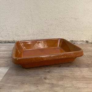 Puede incluir: Una fuente de horno rectangular de cerámica marrón con acabado brillante. La fuente tiene un borde ligeramente elevado y está colocada sobre una superficie de madera. El color es un tono cálido y terroso, apto para el horno.