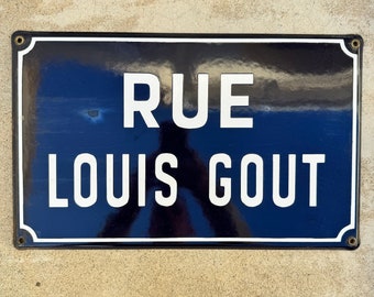 May include: A blue and white enamel street sign with the text "RUE LOUIS GOUT" in white lettering.