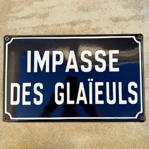 May include: A black and white enamel sign with rounded corners and gold screws. The sign reads "Impasse des Glaïeuls".