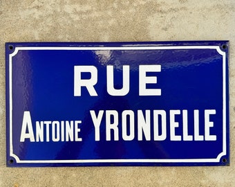May include: A blue enamel street sign with white lettering that reads "RUE ANTOINE YRONDELLLE".